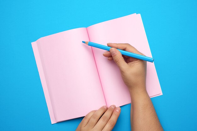 Two female hands holding open notepad with empty pink sheets, top view