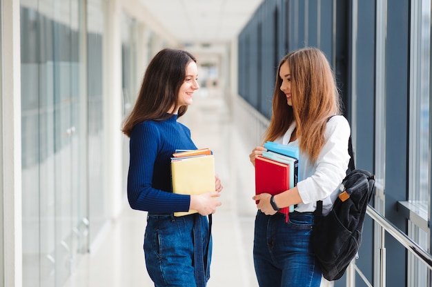 Two female students stand in the corridor of the college with books