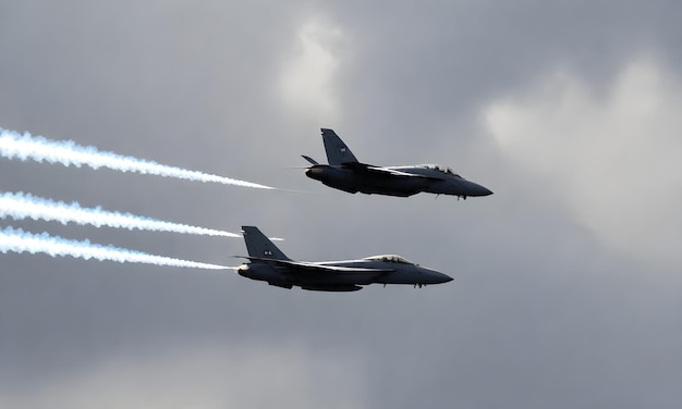 Two fighter jets in flight with contrails against a gray sky