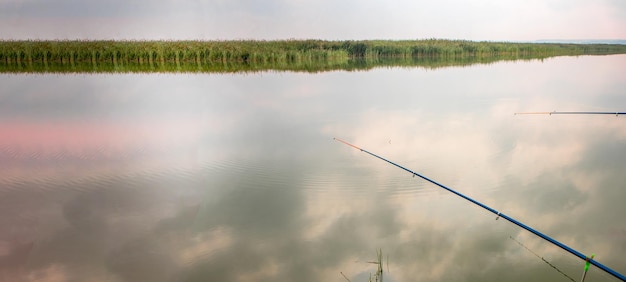 Two fishing rods reflected in the water surface the reflection of clouds Quiet hobby banner