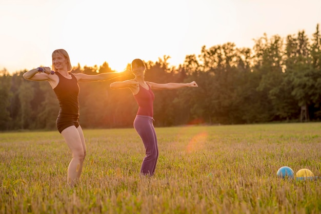 Two fit young women working out with dumbbells standing in the middle of beautiful autumn grassland