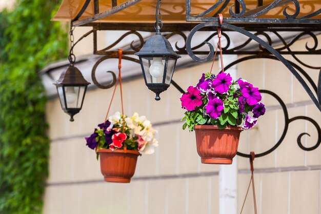 Two flower pots and two lanterns hanging from a metal porch structure