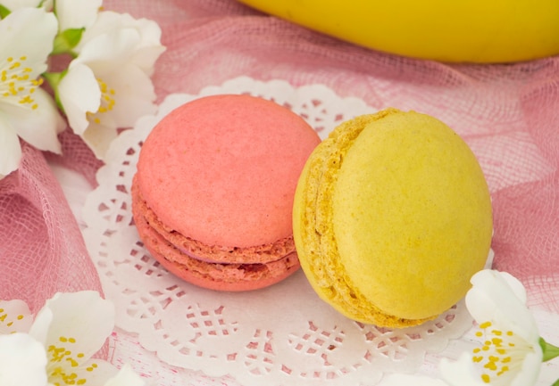 two french macaroons pink and yellow on a pink background with flowers and a banana