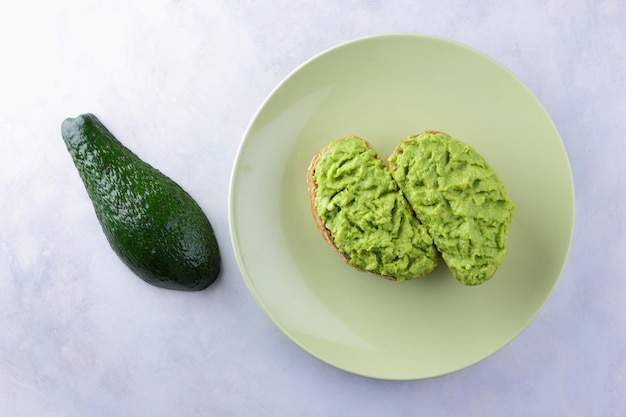 Two fresh green avocado toasts on a green plate Toasts and half avocado isolated on white background Closeup View from above