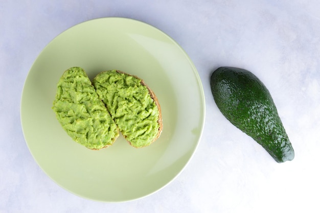 Two fresh green avocado toasts on a green plate Toasts and half avocado isolated on white background Closeup View from above