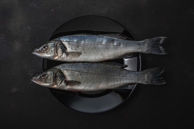 Two fresh seabass fishes on a black plate