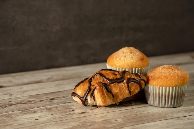 Two freshly baked muffins and a chocolate croissant in the foreground breakfast snack pastry concept