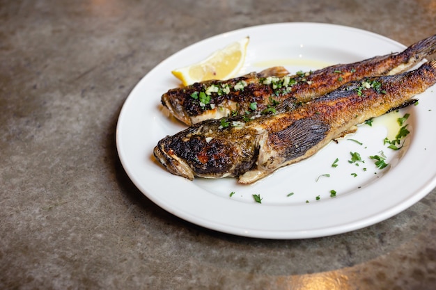 Two fried sea goby fish on white plate with lemon closeup