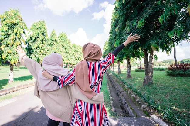 Two friends enjoying the summer sun and holding hand walking in the park shoot from the back