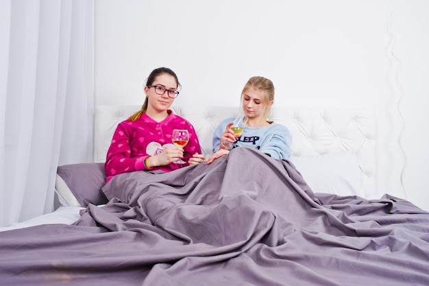 Two friends girls in pajamas having fun on bed at room