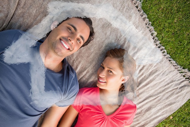 Two friends looking towards the sky while lying on a quilt against house outline in clouds