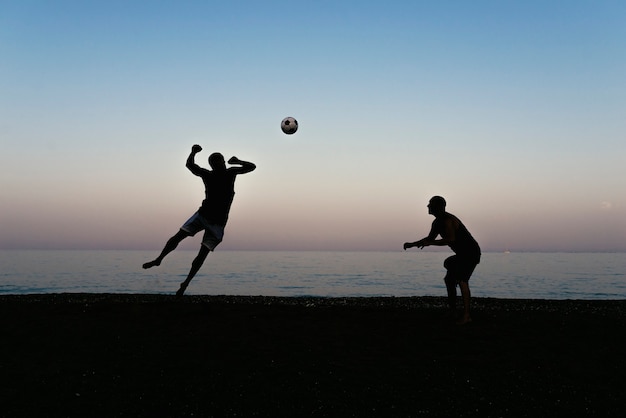 Two friends playing soccer in the beach.