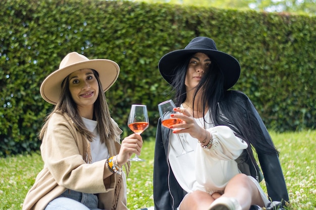 Two friends sitting on the lawn of their garden holding two glasses with champagne and looking at the camera