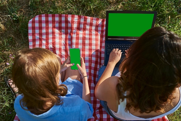 Two friends sitting in a park with a laptop.