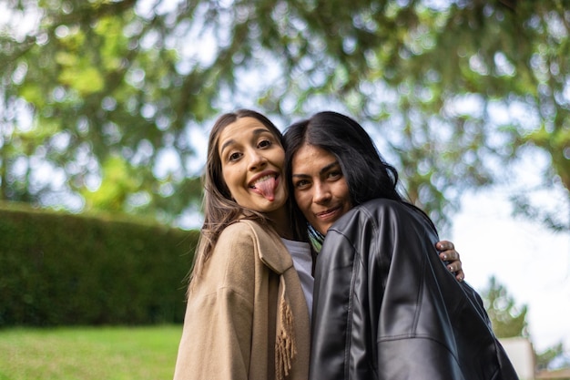 Two friends together happily looking at the camera with tree branches behind them