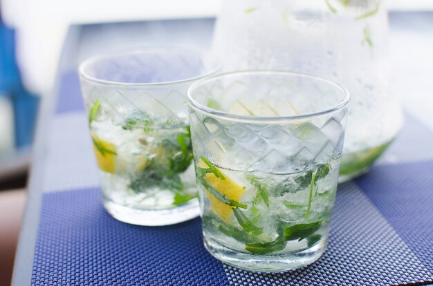 Two full glasses of fresh cool transparent water with ice, lemon and , basil leaves