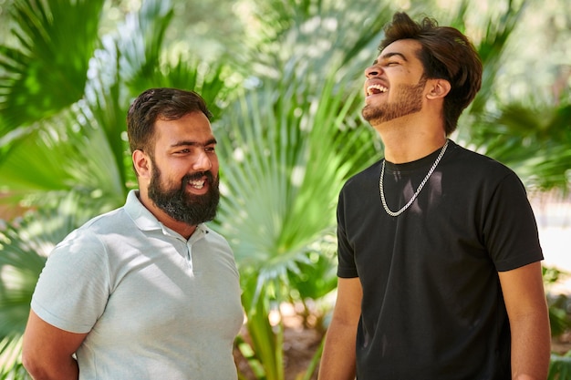 Two funny indian men laughing and speak Hindi in public park green palm leaves background