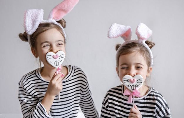 Two funny little sisters are posing with Easter gingerbread in the form of bunny faces