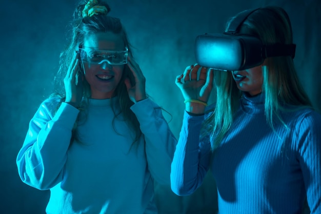 Two futuristic women in vr glasses enjoying virtual reality blue background