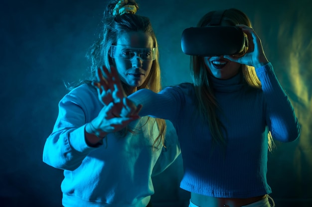 Two futuristic women in vr glasses looking at the metaverse blue background