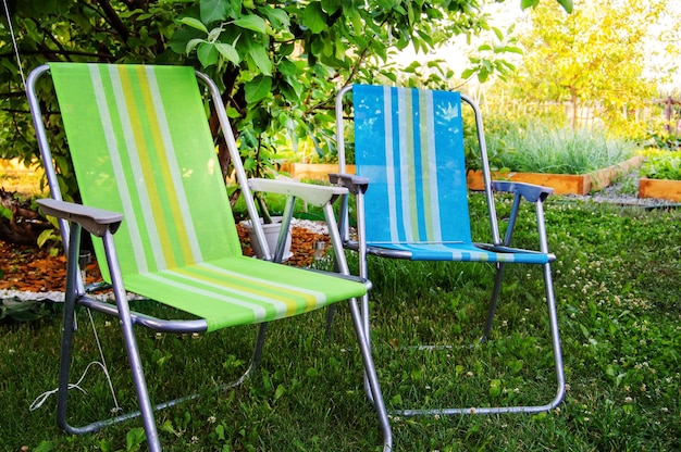 Two garden folding chairs stand in the shade under a tree on a hot summer day in the garden closeup