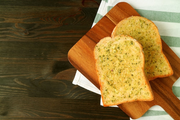 Photo two garlic butter toasts on wooden plate served on dark brown table with napkin