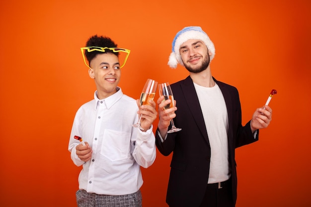 Two gay friends with a Santa hat and star glasses with party horns and champagne glasses