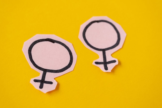 Two gender symbols Venus cut from pink paper on yellow background