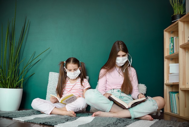 A two girl in medical mask siting on wood floor and reading a books during quarantine