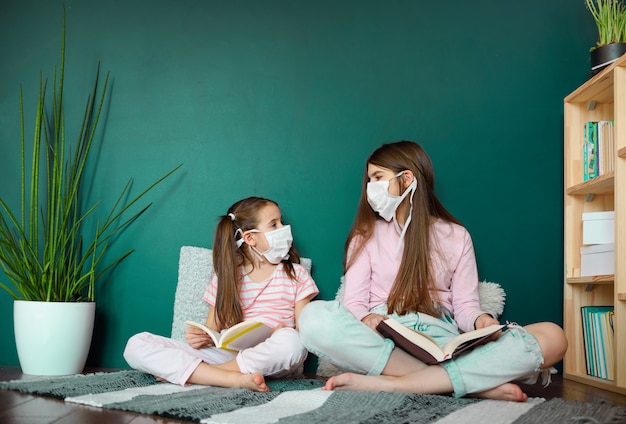 A two girl in medical mask siting on wood floor and reading a books during quarantine