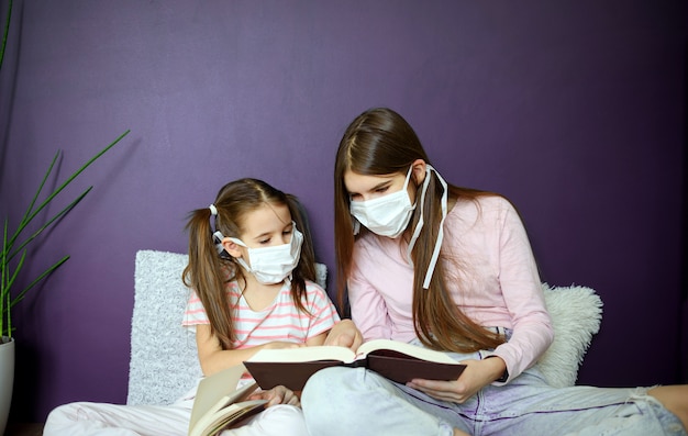 A two girl in medical mask siting on wood floor and reading a books during quarantine