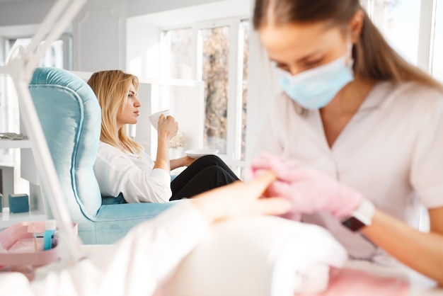 Two girlfriends relax on pedicure procedure in beauty salon. Professional beautician and female customers, nail care in spa