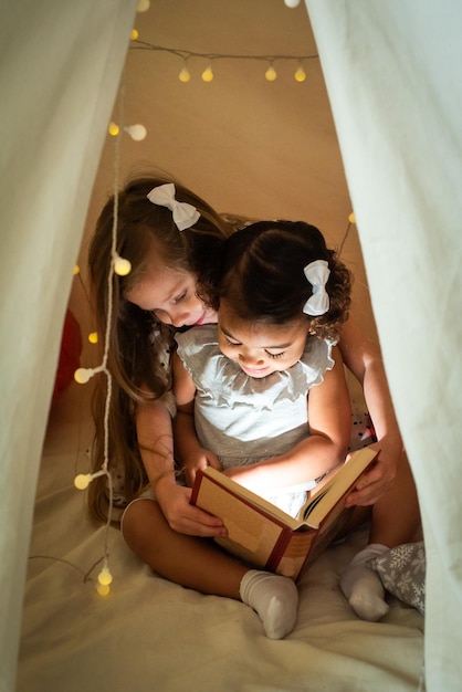 Two girls are reading a book in a tent with a garland baby with black and white skin color study