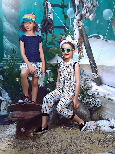 Two girls are sitting on a rock and one is wearing sunglasses and the other is wearing a blue shirt.