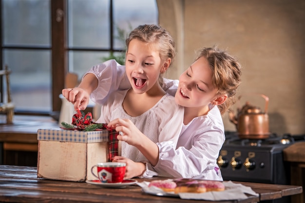 two girls cheerfully untie the ribbon on the gift box in the cozy kitchen at home