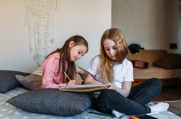 Two girls friends play at home draw with pencils and felttip pens and have fun