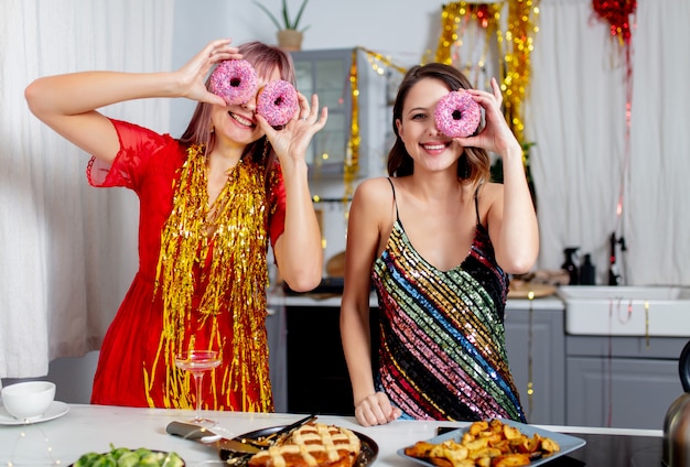 Two girls having fun with donuts in the kitchen after a party