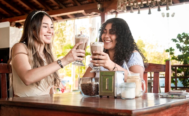 Two girls having a milkshake two girl friends in a cafe two girls toasting in a cafe