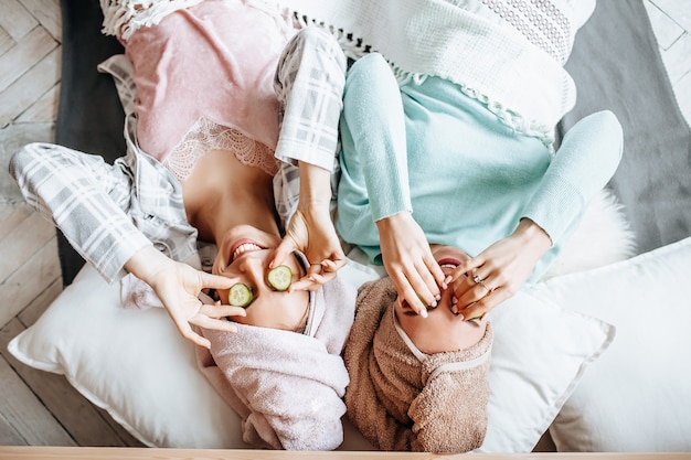 Two girls make homemade face and hair beauty masks with cucumber