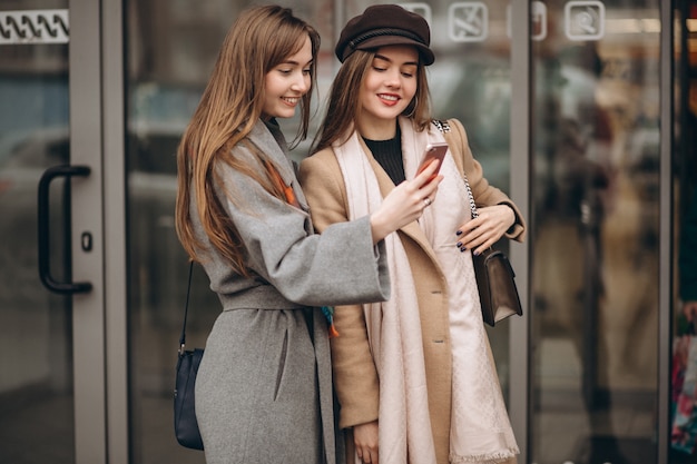 Two girls outside shopping mall with phone in an autumn day