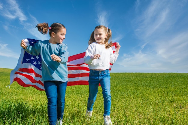 Two Girls Running Through A Green Meadow With A Blue Sky,Showing The Flag Of The United States.USA