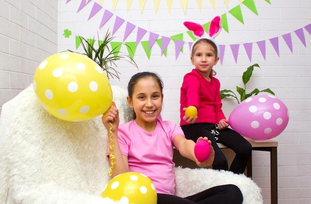 Two girls sisters celebrate easter holiday in room decorated with flags and balloons