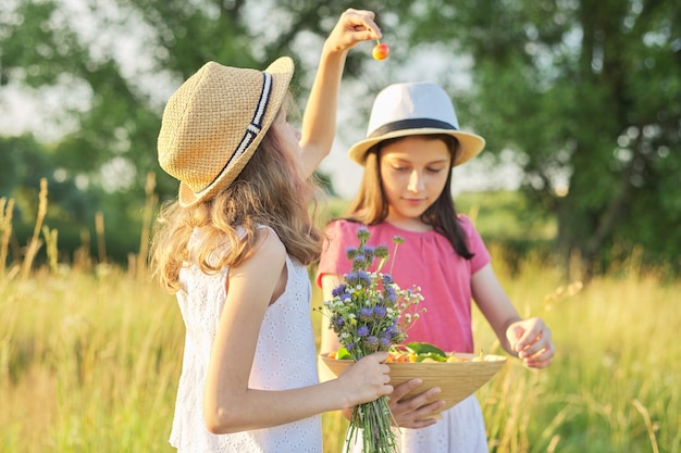 Two girls on sunny summer day in meadow with bowl of sweet fruits