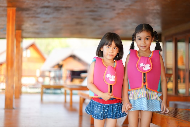 Two girls in swimming suit and life jacket hold hand together