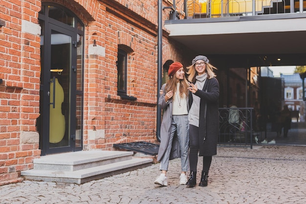 Two girls walking on street together and holding their hands they are wearing spring or autumn