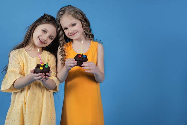 Two girls with cupcakes and festive candles on a bright background