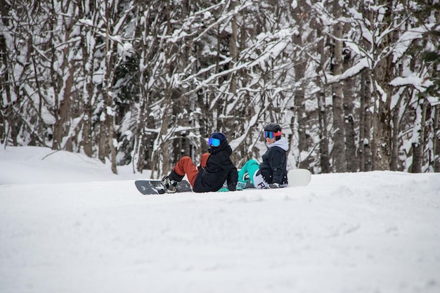 Two girls with a snowboards sits on the side of the mountain