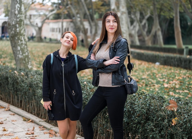 Two girls - young lesbian couple walking in autumn park and making fun. Portrait of a smiling young lesbian couple hugging each other while standing together on city street