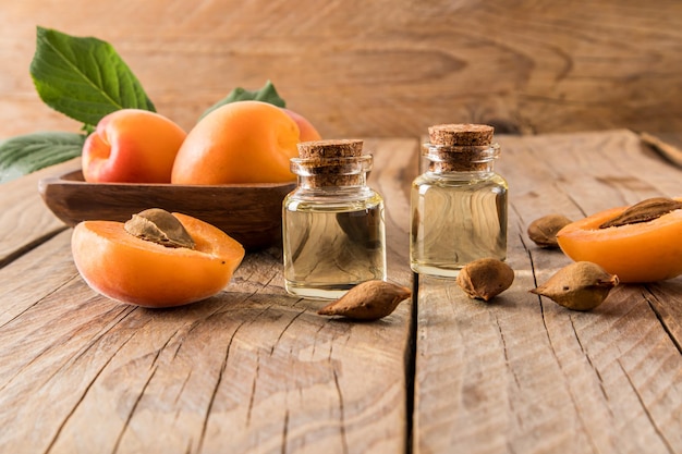 Two glass bottles of apricot kernel oil on a wooden village table against a backdrop of ripe fruit the concept of natural organic selfcare