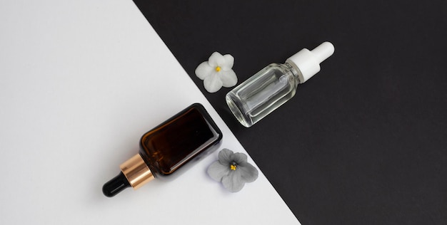 Two glass bottles with aromatic oil or serum with flowers nearby Natural organic cosmetic Spa concept Front view